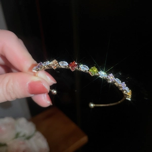 Detailed close-up of a gold open bracelet featuring multicolored zircon stones in hand