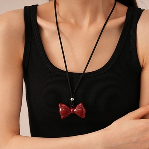 Detail of red resin bow pendant on black cord necklace worn on a black ribbed top