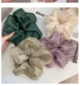 Detail of four large pleated silk scrunchies in peacock green and champagne tones