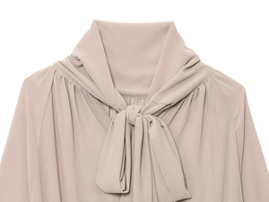 Primer plano detallado de blusa de gasa color albaricoque con lazo en cuello y hombro plisado
