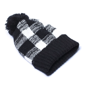 Detail of winter knit beanie with black and white checkerboard pattern and faux fur pom