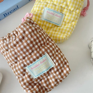 Detail of yellow and brown quilted camera bags with pink drawstrings on white surface