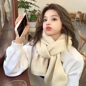 Detailed close-up of cream knit scarf with fashion label on female model in a cafe