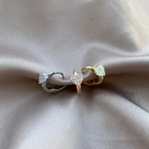 Detailed view of heart-shaped huggie earrings in silver, rose gold, and gold on satin