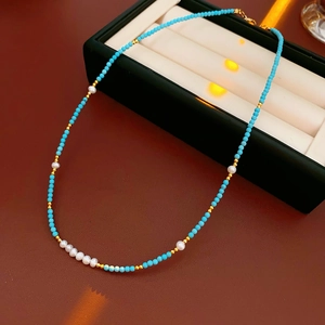Detail of turquoise and freshwater pearl necklace on display with gold bead accents