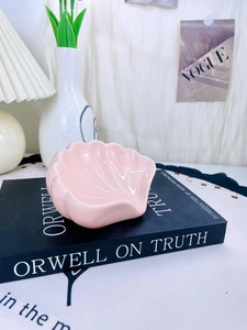 Primo piano di un vassoio per gioielli in ceramica rosa a forma di conchiglia su un libro