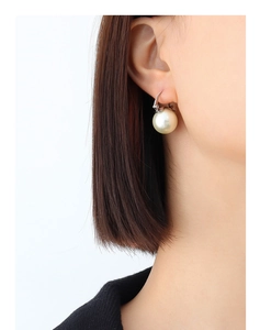 Gros plan d'une grande boucle d'oreille perle blanche avec crochet argenté sur un modèle