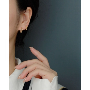 Detail of twisted gold leaf earrings with a sparkling gemstone worn on an ear