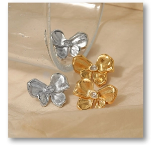 Macro shot of bow earrings with brushed texture and drop-shaped zircon on fabric