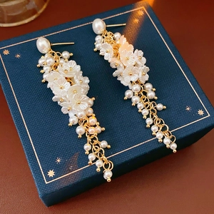 Detail of long floral tassel earrings with pearls and golden petals on navy jewelry box