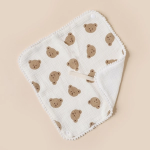 Detail of white cotton baby bib with brown bear print and pom-pom trim texture