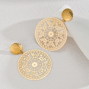 Close-up of vintage golden hollow engraved round earrings with hammered texture on fabric