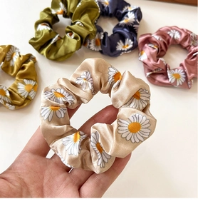 Close-up of five daisy print satin scrunchies in beige olive pink navy and yellow