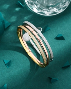 Close-up of tricolor bangle set with a micro-paved zircon safety pin charm detail