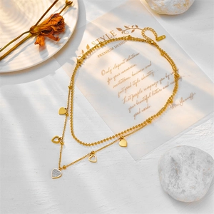 Double-layered gold heart necklace with zircon accents on a chic white wooden surface