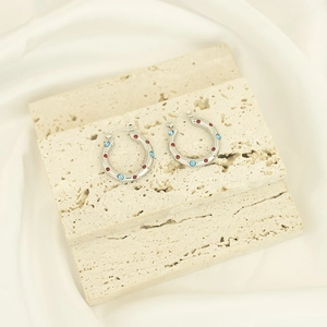 Macro detail of silver steel hoop earrings set with red and blue zircon on stone