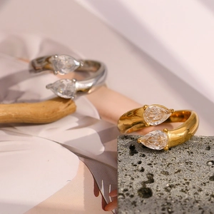 Detail of 18K gold and silver teardrop zircon rings on natural stone and wood