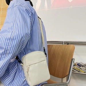 Minimalist white nylon crossbody bag with front zipper pocket shown on model