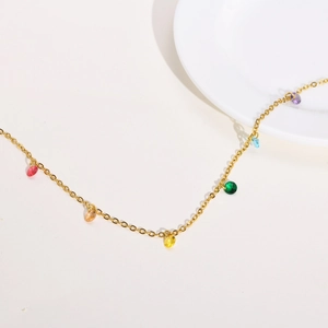 Detailed view of golden necklace with multi-colored zircon teardrop pendants on white flat lay