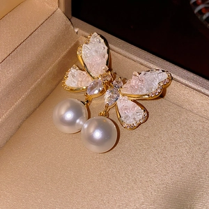 Macro shot of asymmetric butterfly pearl earrings with gold base and zircon accents