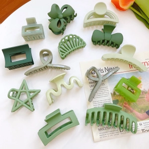 Flat lay of green matte resin hair clips in various geometric and bow shapes on newspaper