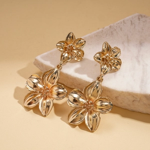 Close-up of golden metallic flower earrings on marble surface with soft natural lighting