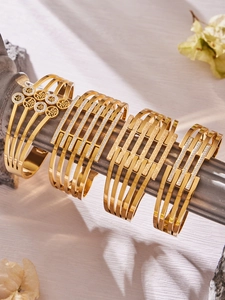 Dettaglio di quattro bracciali geometrici dorati con cristalli pavé su display grigio