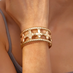 Detailed view of wide gold-toned cutout cuff bracelet with clover patterns and bead edges