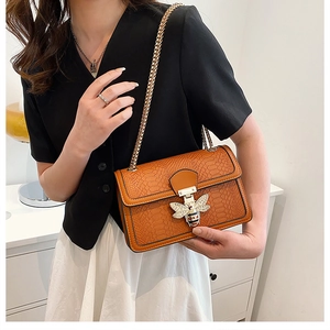 Detail of crossbody bag with embossed snake pattern leather and golden bee metal clasp