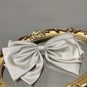 Close-up of elegant beige silk bow hair clip on a vintage mirror with satin texture