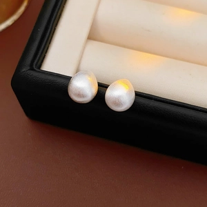 Detailed close-up of matte white teardrop pearl earrings inside a black leather jewelry box