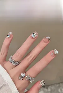 Detail of silver press-on nails with 3D crystal bows, pearls and sparkling glitter finish