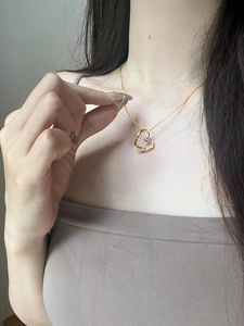 Detailed view of a gold-toned twisted heart pendant necklace worn on a woman's collarbone