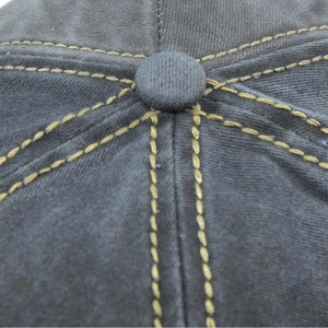 Macro detail of dark grey cotton baseball cap top button and yellow stitching