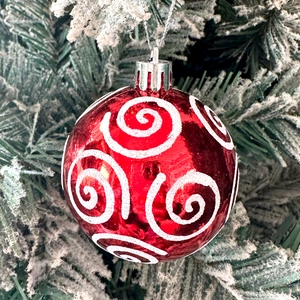 Close-up of red Christmas ornament with white glitter swirls on snowy pine tree