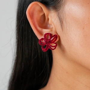 Gros plan sur les boucles d'oreilles fleurs floquées bordeaux avec texture mate sur modèle