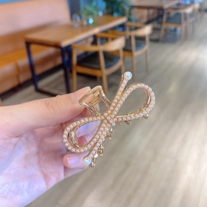 Detail of a golden metal butterfly hair claw clip with pearls held in a person's hand