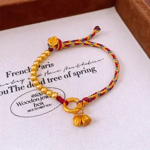 Handmade woven Chinese bracelet with lotus pendants and golden beads on a display tray