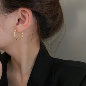 Close-up of minimalist gold hoop earrings on a model wearing a black blazer jacket