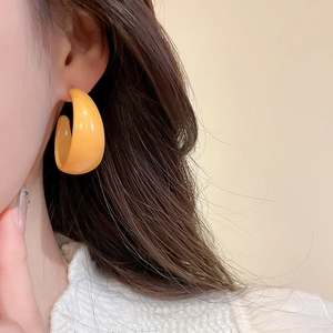 Close-up of bright orange acrylic C-shaped hoop earrings on a model with glossy finish