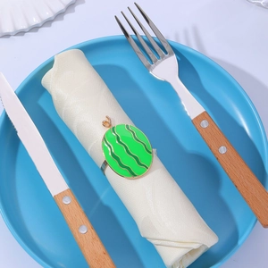 Close-up of watermelon napkin ring on white fabric with wooden cutlery on blue plate