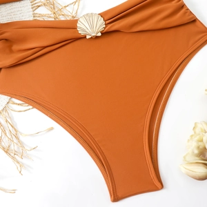 Close-up of burnt orange high-waisted bikini bottom with shell charm and ruched details