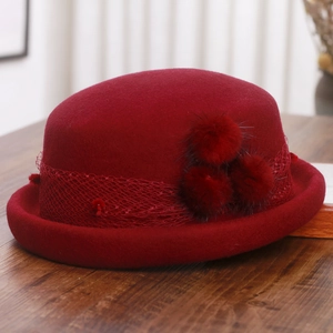 Detail of burgundy wool beret with elegant mesh veil and soft plush pom-pom accents