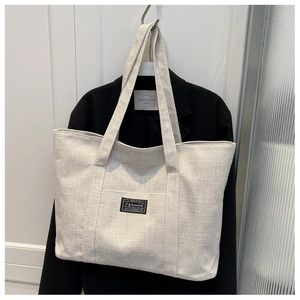 Detail of canvas tote bag showing fashion label and reinforced stitching on handle
