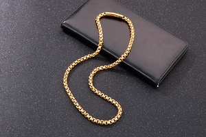 Macro detail of men's golden round box chain necklace with cylindrical push lock closure