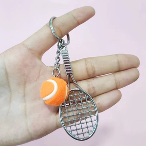 Mini tennis racket and orange ball keychain for bags shown in high detail on pink background
