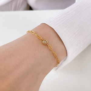 Detail of gold chain bracelet with a round clear gem worn on a female wrist
