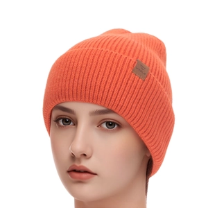 Detailed view of bright orange ribbed knit beanie featuring a brown leather brand patch