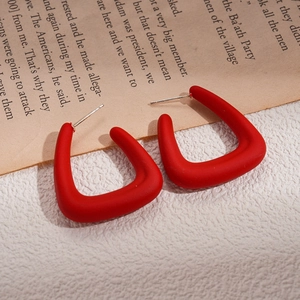 Macro view of matte red acrylic C-shaped earrings on a vintage newspaper background