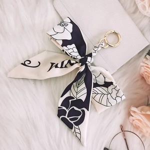 Detail of floral silk scarf keychain with gold ring on white plush background